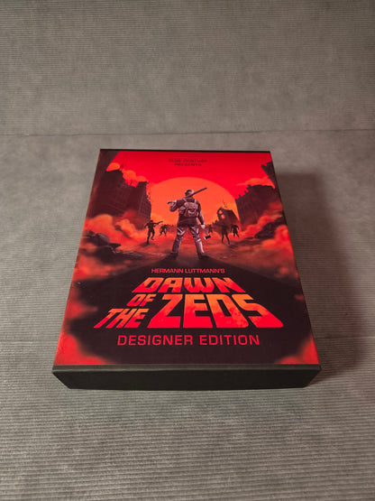 Board game box titled 'Dawn of the Zeds' on a gray surface